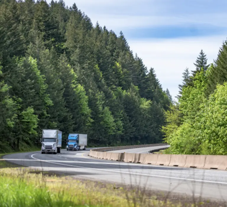 Two semi trucks driving down a highway with green trees on each side